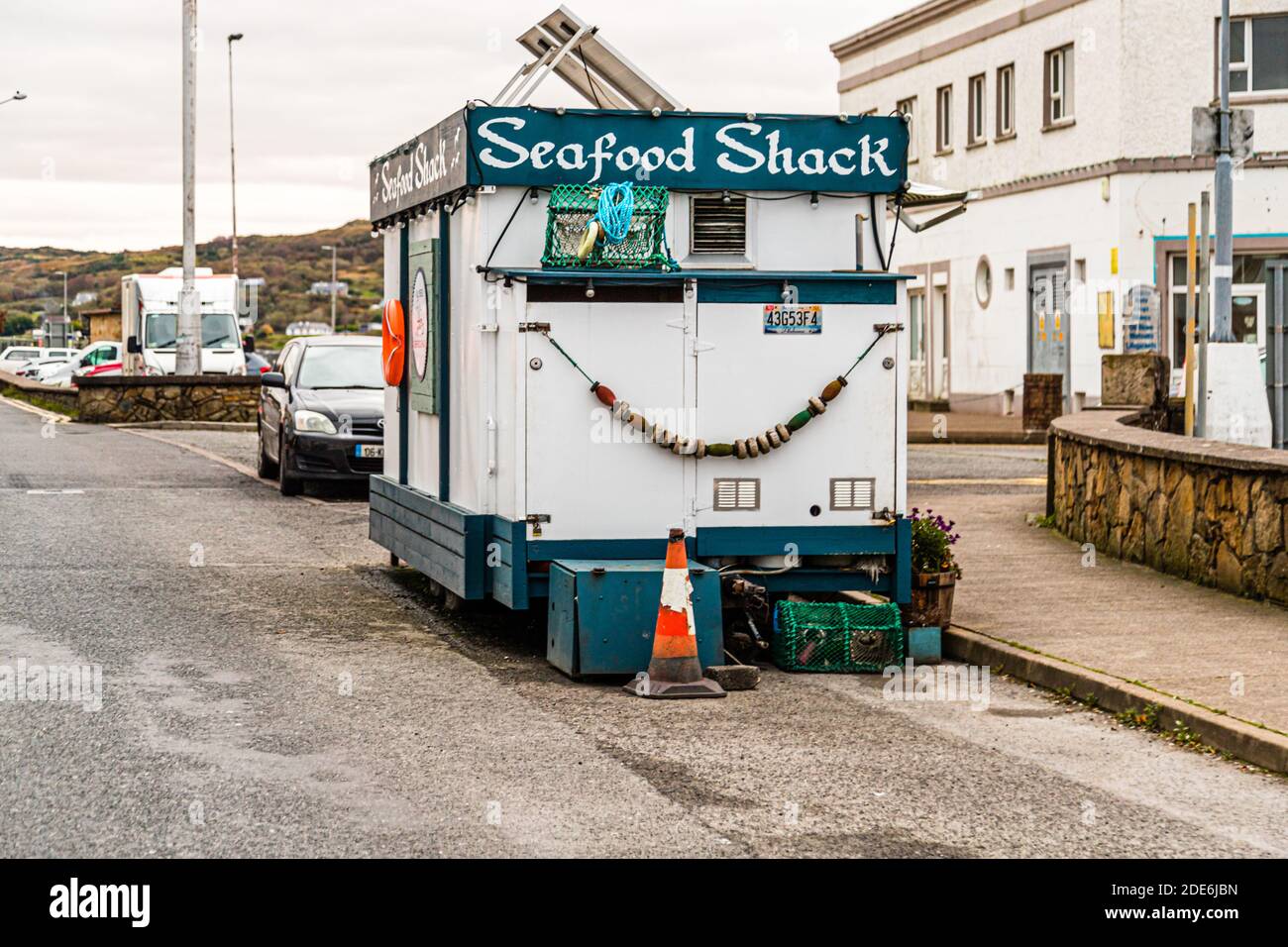 A mobile food trailer marked "Seafood Shack" stands at the pier in Killybegs, County Donegal, Ireland. Green fishing net gear and a shell garland hang on its outer wall. Stock Photo