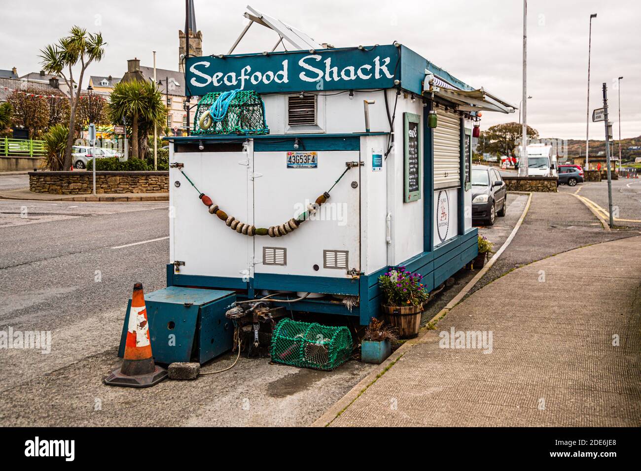 The "Seafood Shack" food trailer stands at the pier in Killybegs, County Donegal, Ireland, with a view of the town and a church tower in the background. Stock Photo