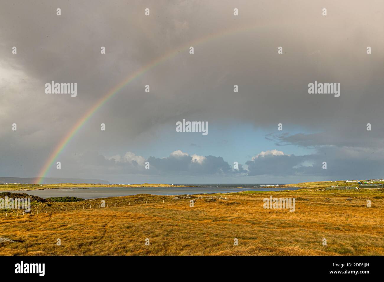 A rainbow arches over the hilly landscape along the R259 road in County Donegal, Ireland. Meadows and pastureland line the green scenery on either side of the road. Stock Photo