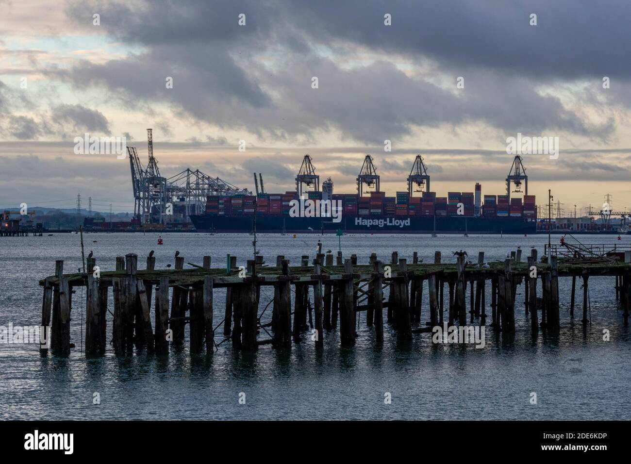 a large container ship at the port of southampton at sunset with docks cranes in silhouette. Stock Photo