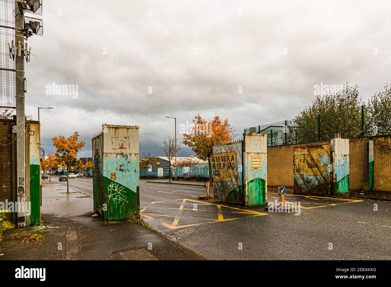 The gates at Lanark Way between Clonard and the Shankill Road, Belfast, Northern Ireland, display, seen from across the road, the lettering "... is never a [war] or a bad [pe]ace" on rusted metal, surrounded by graffiti. Stock Photo