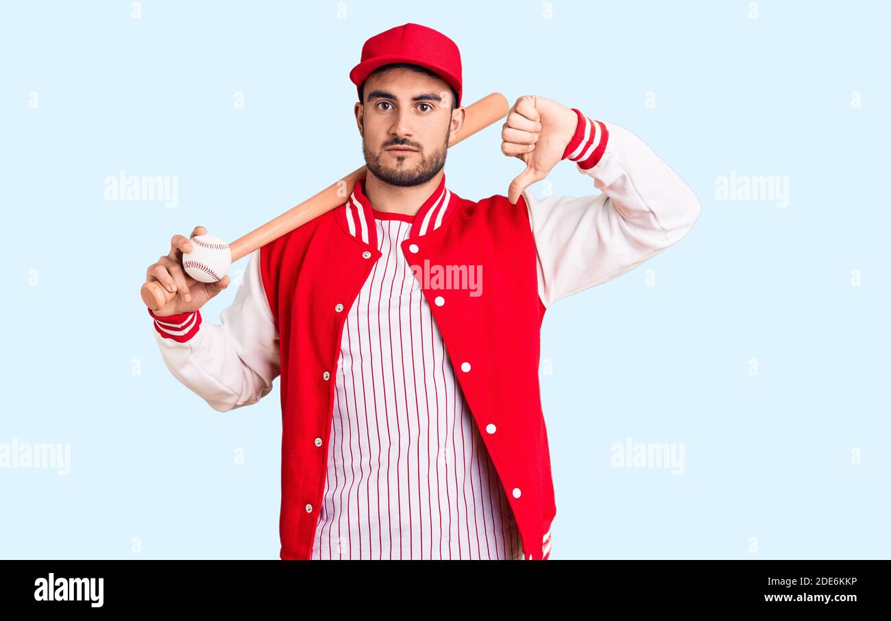 Young handsome man holding baseball bat and ball with angry face