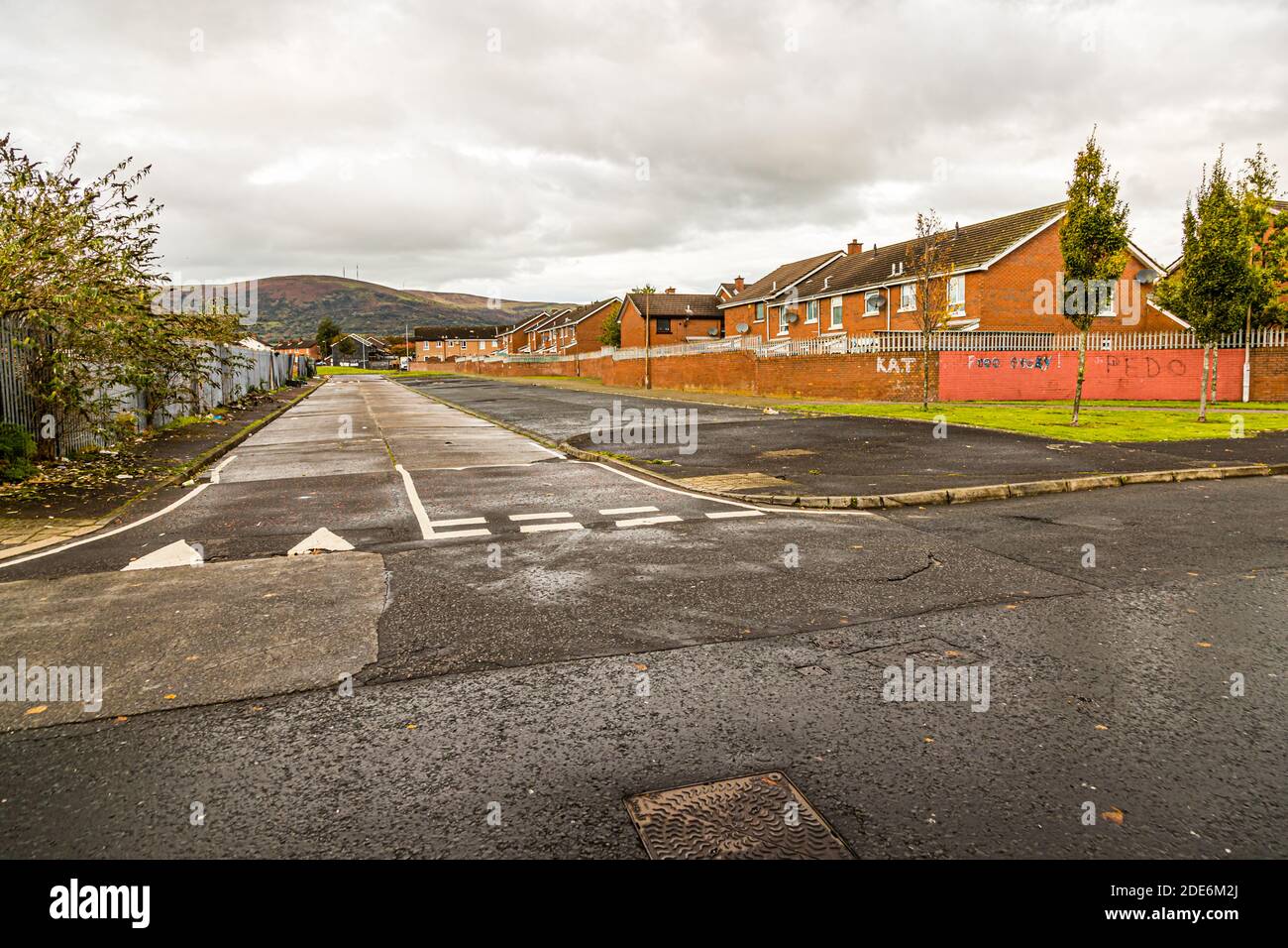 A residential street on North Howard Street, Belfast, Northern Ireland, runs between terraced houses towards the hills on the edge of the city; a brick wall in the foreground bears crude graffiti scrawls. Stock Photo