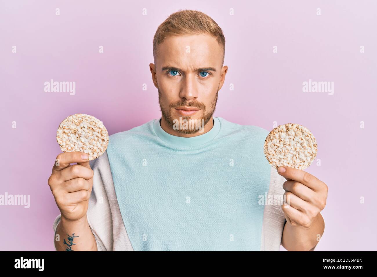 Young caucasian man eating healthy rice crackers skeptic and nervous, frowning upset because of
