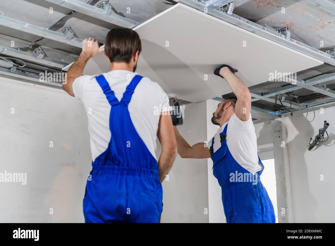 Foremen in blue overalls stand on a ladder and make a ceiling Stock Photo