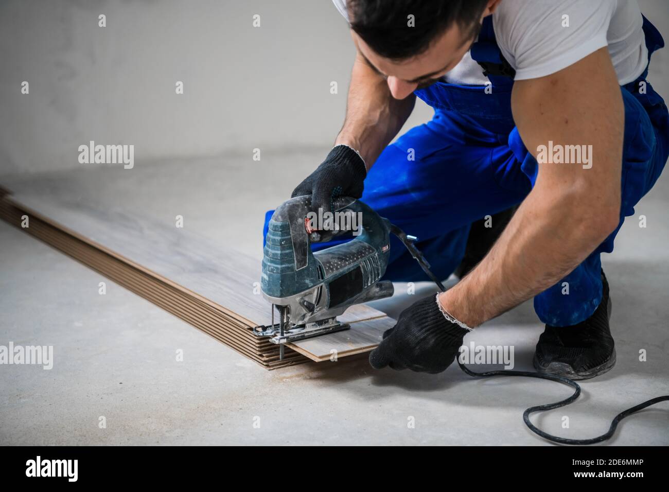 Woodworker in blue work clothes sawing laminate boards with an electric
