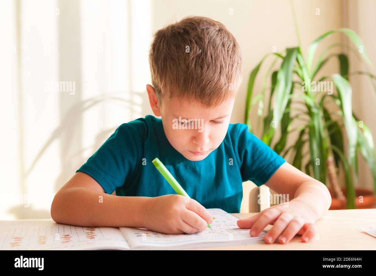 7 years old child boy doing lessons sitting at desk in his room Stock