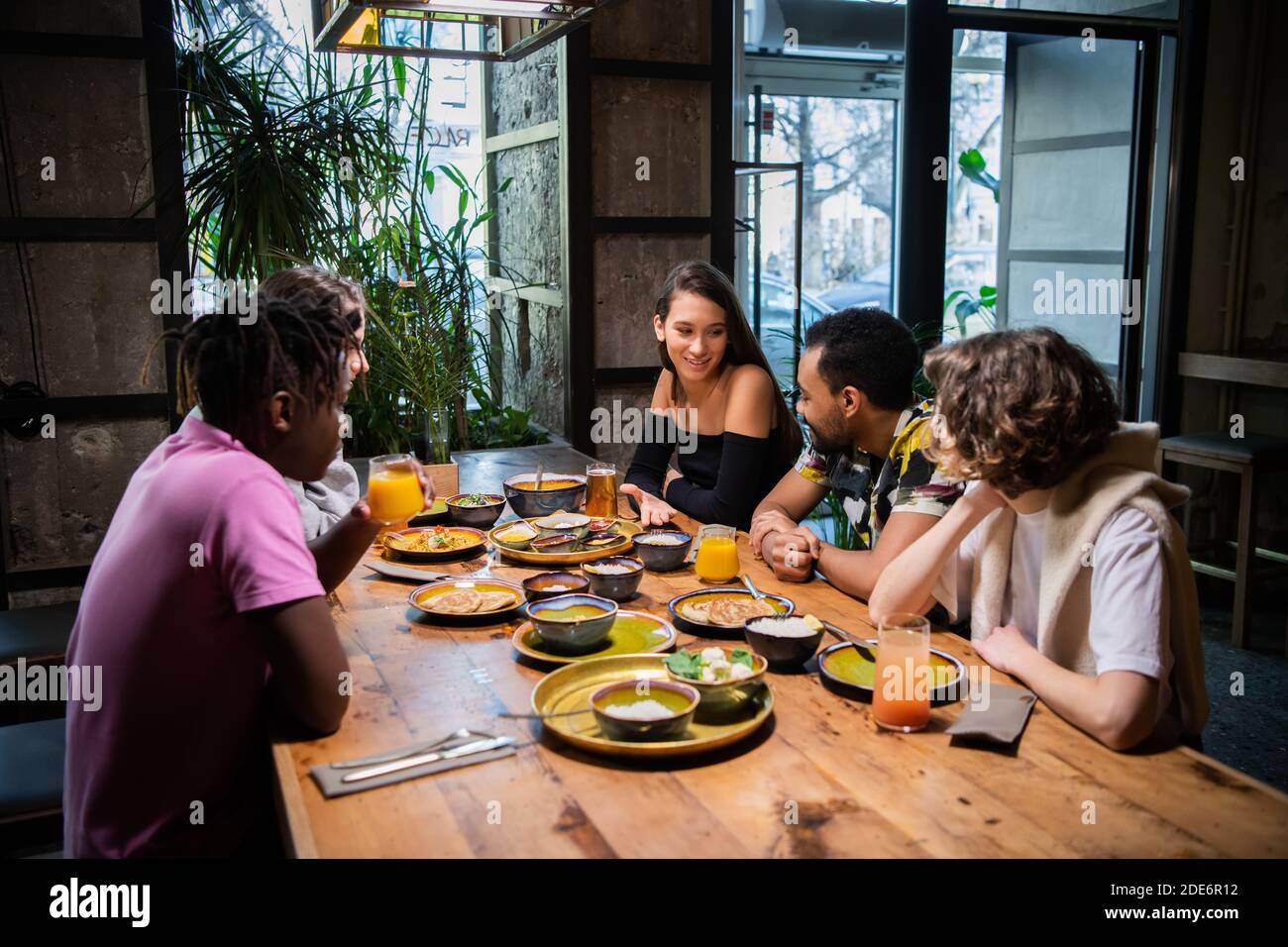 A multicultural group of young people in a cafe, eating asian food, drinking cocktails, chatting. Stock Photo