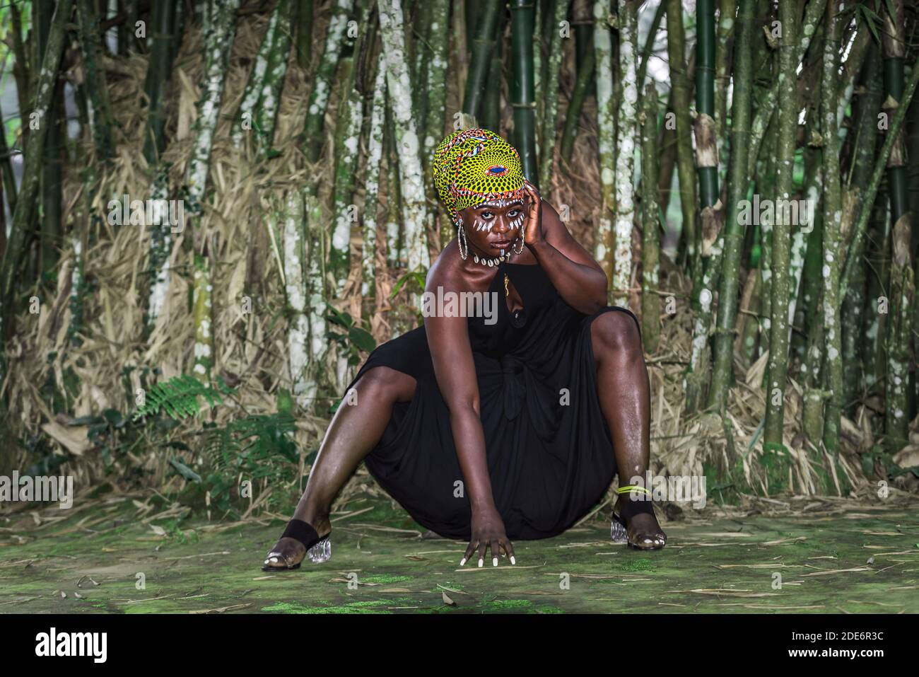 African woman sitting in front of bamboo forest with African face painting in Aburi Ghana West Africa Stock Photo