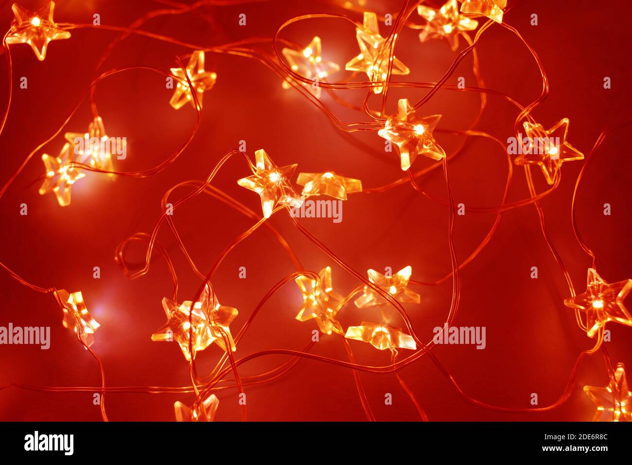Christmas festive garlands in the shape of a star. Glowing festive golden bokeh. Red background for design. Stock Photo