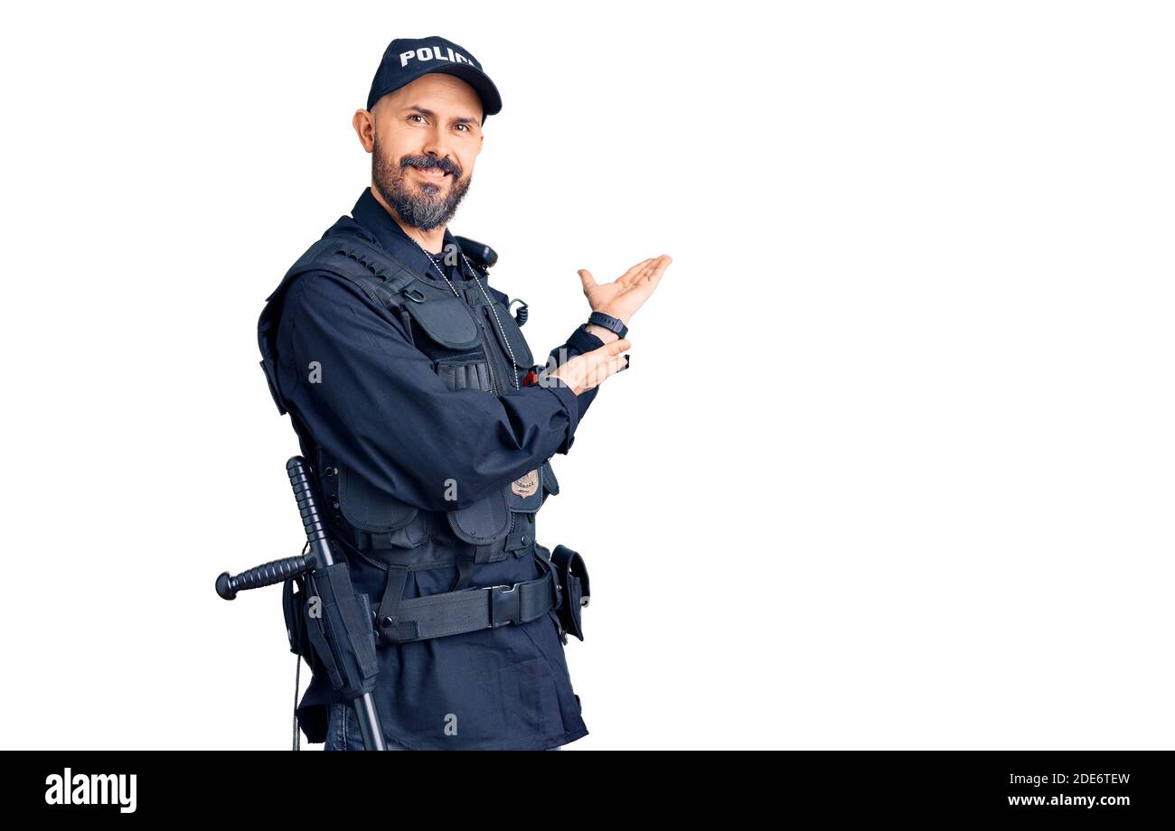 Young handsome man wearing police uniform inviting to enter smiling natural with open hand Stock Photo