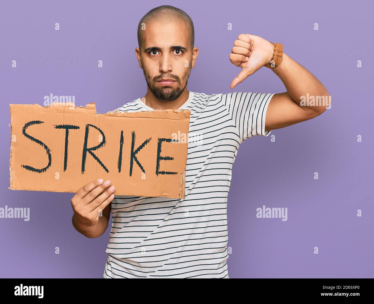 Hispanic adult man holding strike banner cardboard with angry face, negative sign showing dislike with thumbs down, rejection concept Stock Photo