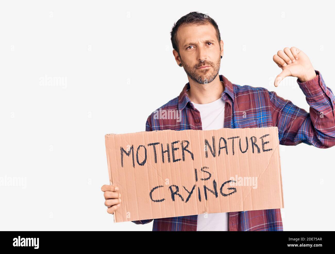 Young handsome man holding mother nature is crying protest cardboard banner with angry face, negative sign showing dislike with thumbs down, rejection Stock Photo