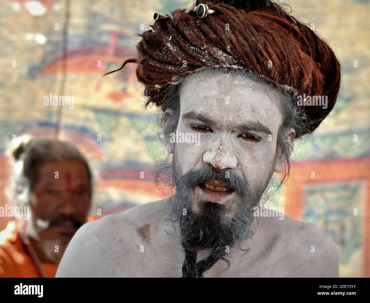 Indian Hindu Shaivite sadhu (baba, yogi) with dread bun and sacred white ash (vibhuti) all over his face, beard and upper body poses for the camera. Stock Photo