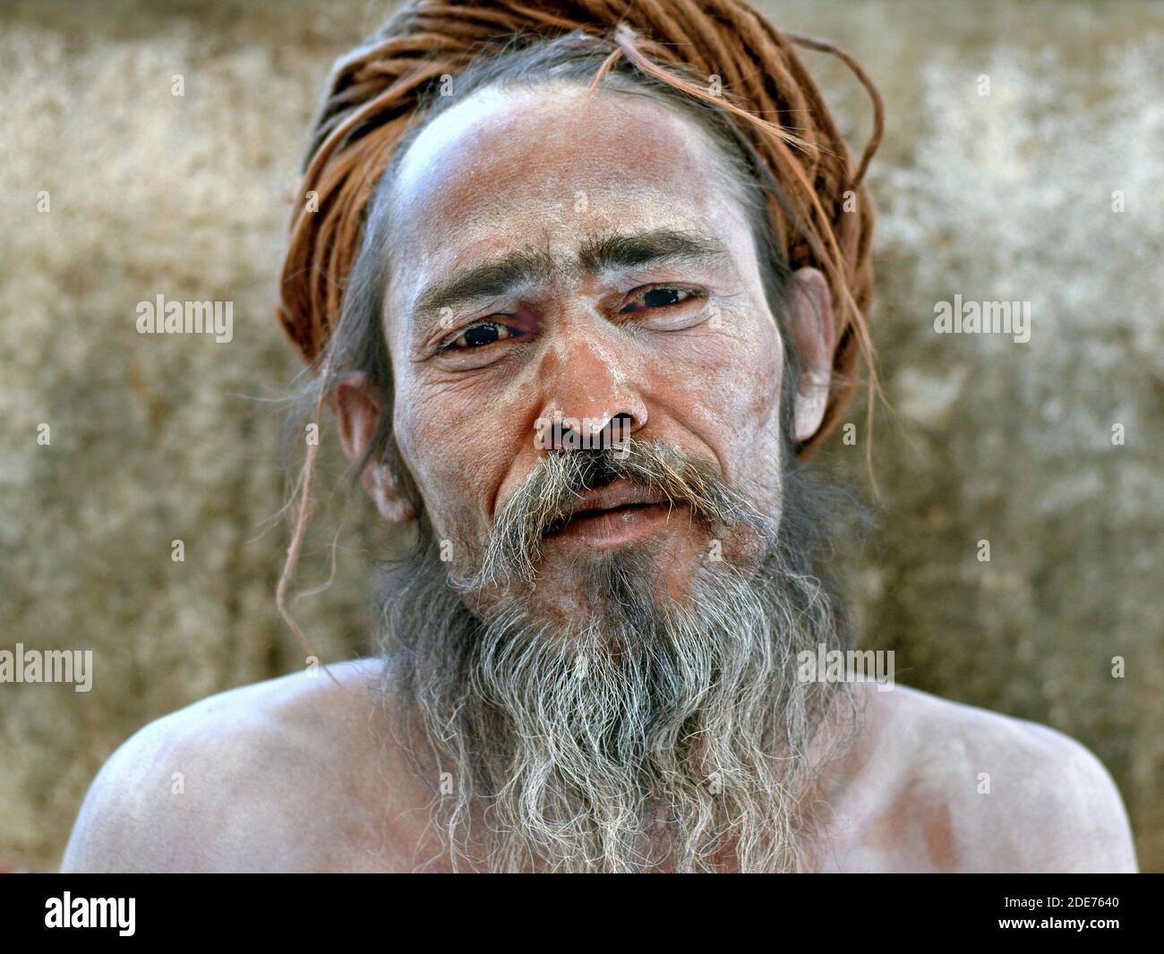 Spiritual Indian Hindu sadhu baba with white sacred ash all over his face and shoulders and with rolled-up long dreadlocks poses for the camera. Stock Photo