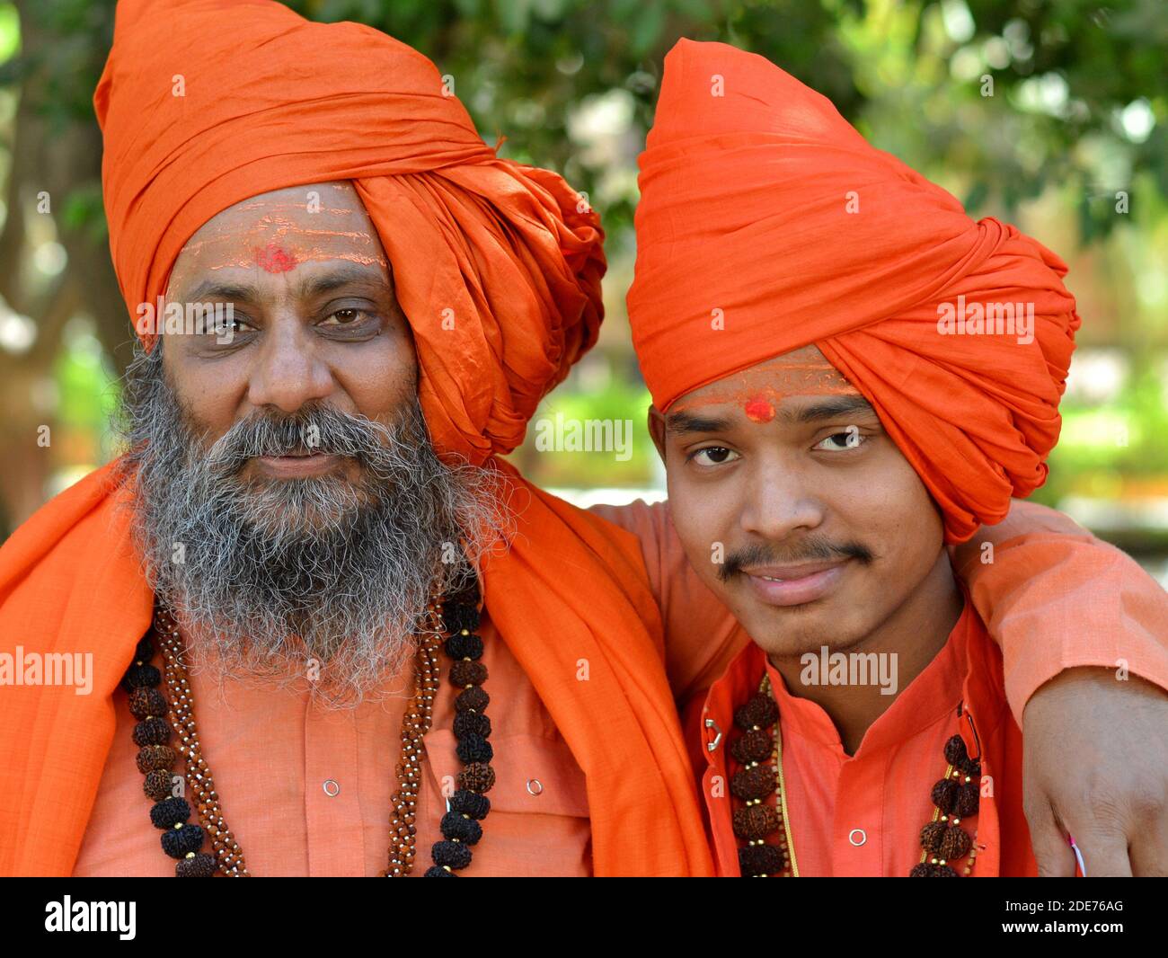 Two Indian Hindu holy men (Shaivite sadhus, monks, devotees), old and young, wear orange outfits and pose together during Maha Shivaratri. Stock Photo