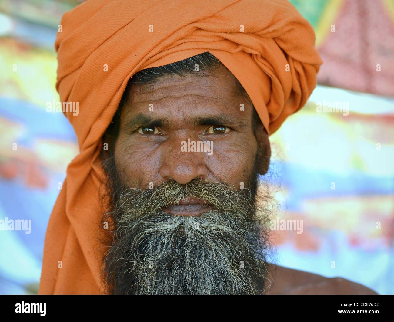Serious looking Indian Hindu holy man (sadhu, baba, guru) wears a saffron colored turban and poses for the camera during Shivratri Mela festival. Stock Photo