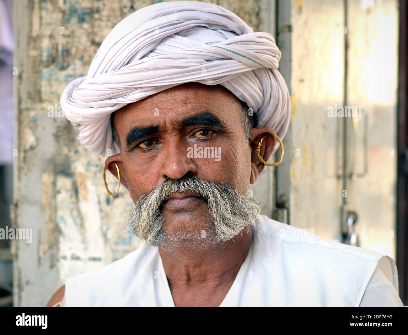 Handsome middle aged Indian Rabari shepherd man with golden tribal earrings wears a white turban and large friendly mutton chops (moustache). Stock Photo