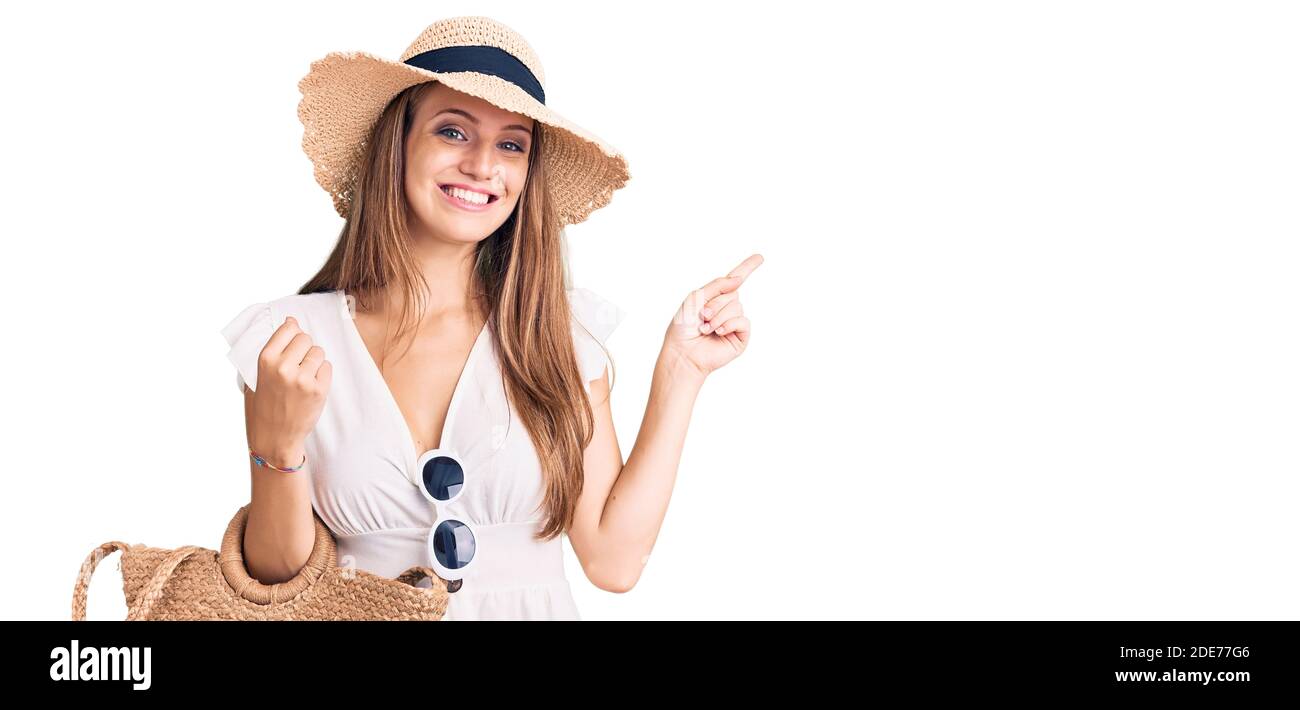 Young beautiful blonde woman wearing summer dress and wicker handbag smiling happy pointing with hand and finger to the side Stock Photo
