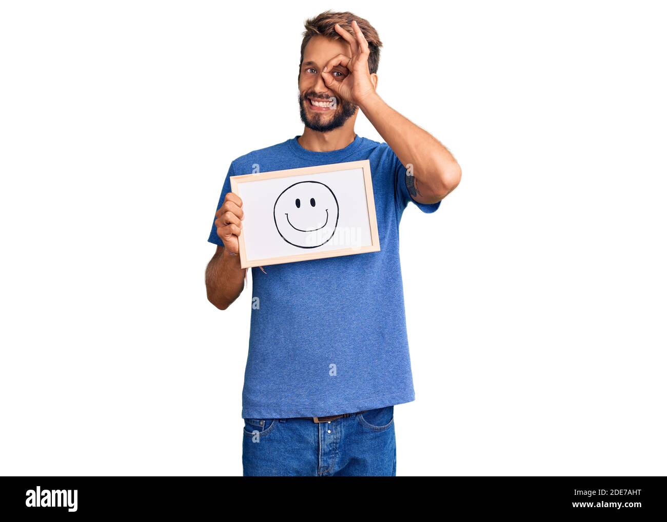 Handsome blond man with beard holding blackboard with happy face smiling happy doing ok sign with hand on eye looking through fingers Stock Photo
