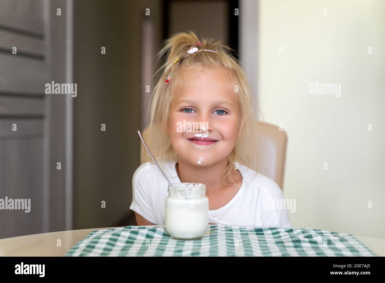 Cute adorable caucasian little funny blond girl eating yogurt or milk