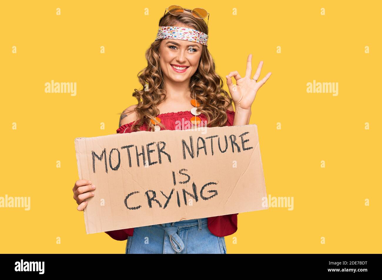 Young blonde girl wearing hippie style holding mother nature is crying  protest cardboard banner doing ok sign with fingers, smiling friendly  gesturing Stock Photo - Alamy