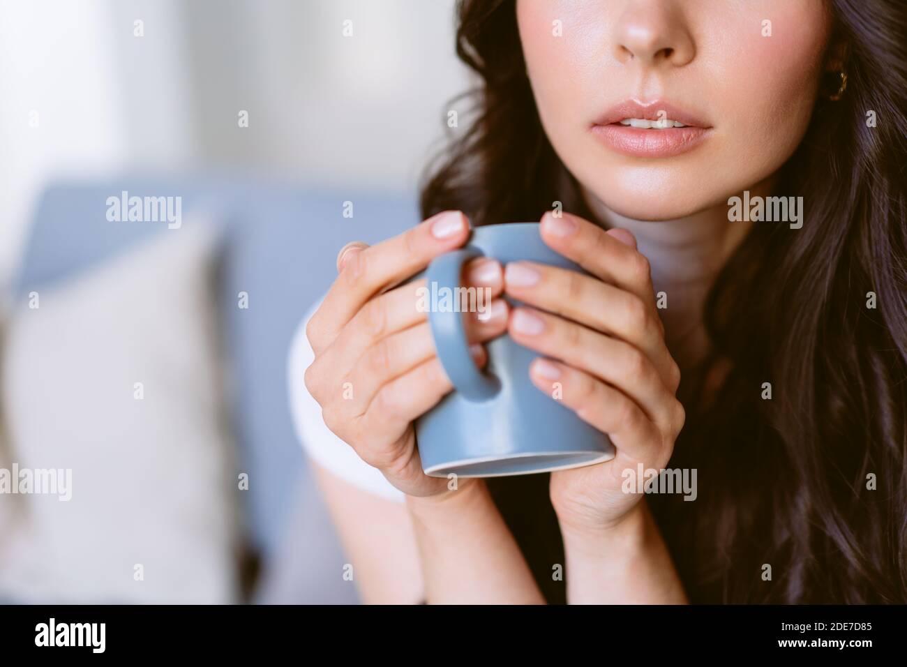 Young woman drinking tea and dreaming sitting on the couch in the bright apartment. Stock Photo