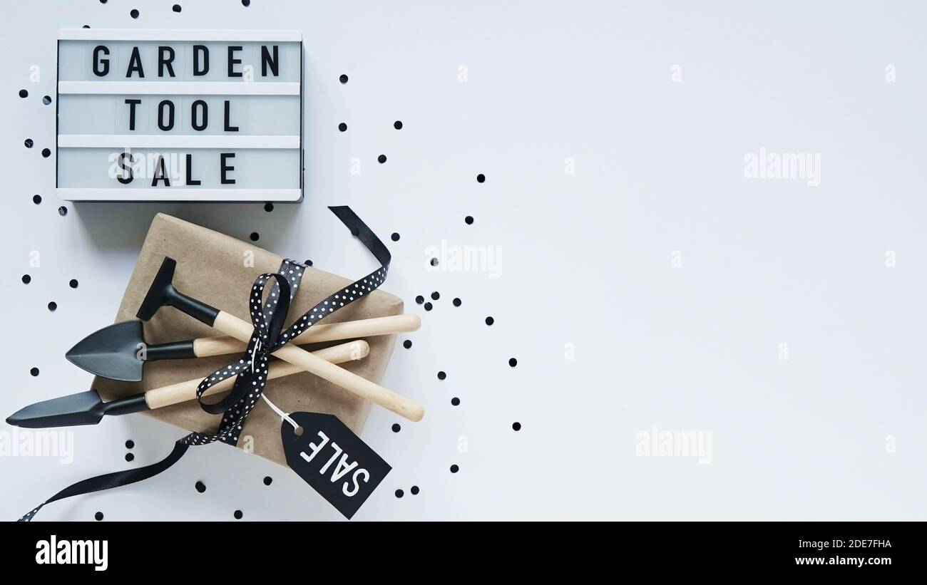 Banner concept for Black Friday celebration,lettering.White board with text GARDEN TOOL SALE, gift box with black pea bow and garden tools,tag,confett Stock Photo