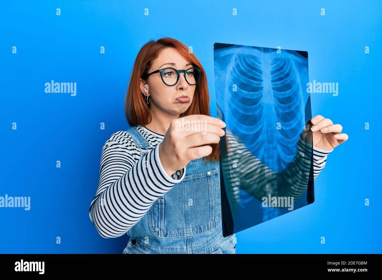 Beautiful redhead woman holding chest radiography depressed and worry ...