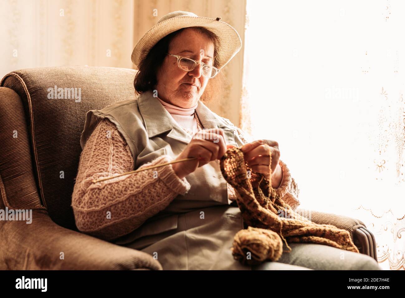 Elderly woman knitting sweater for her grandchildren by the window ...