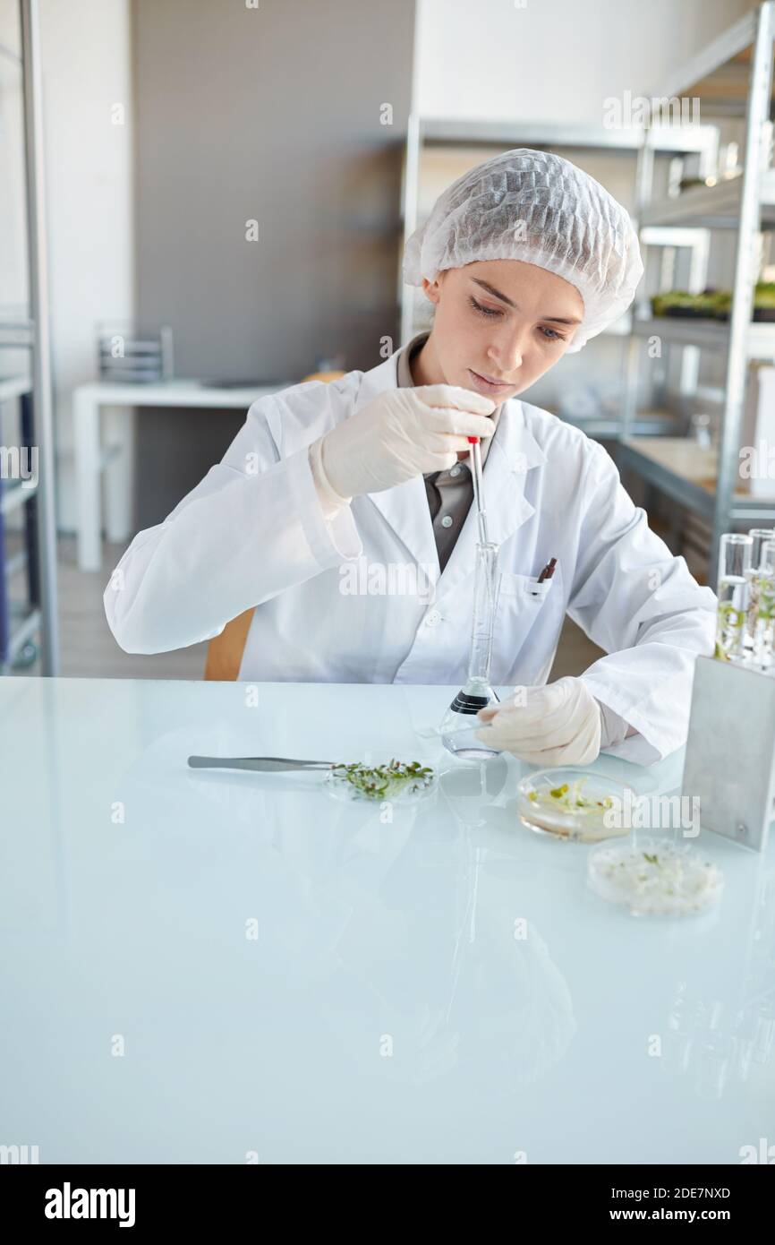Vertical portrait of young female scientist performing experiments with plant samples while working on research in biotechnology lab, copy space Stock Photo