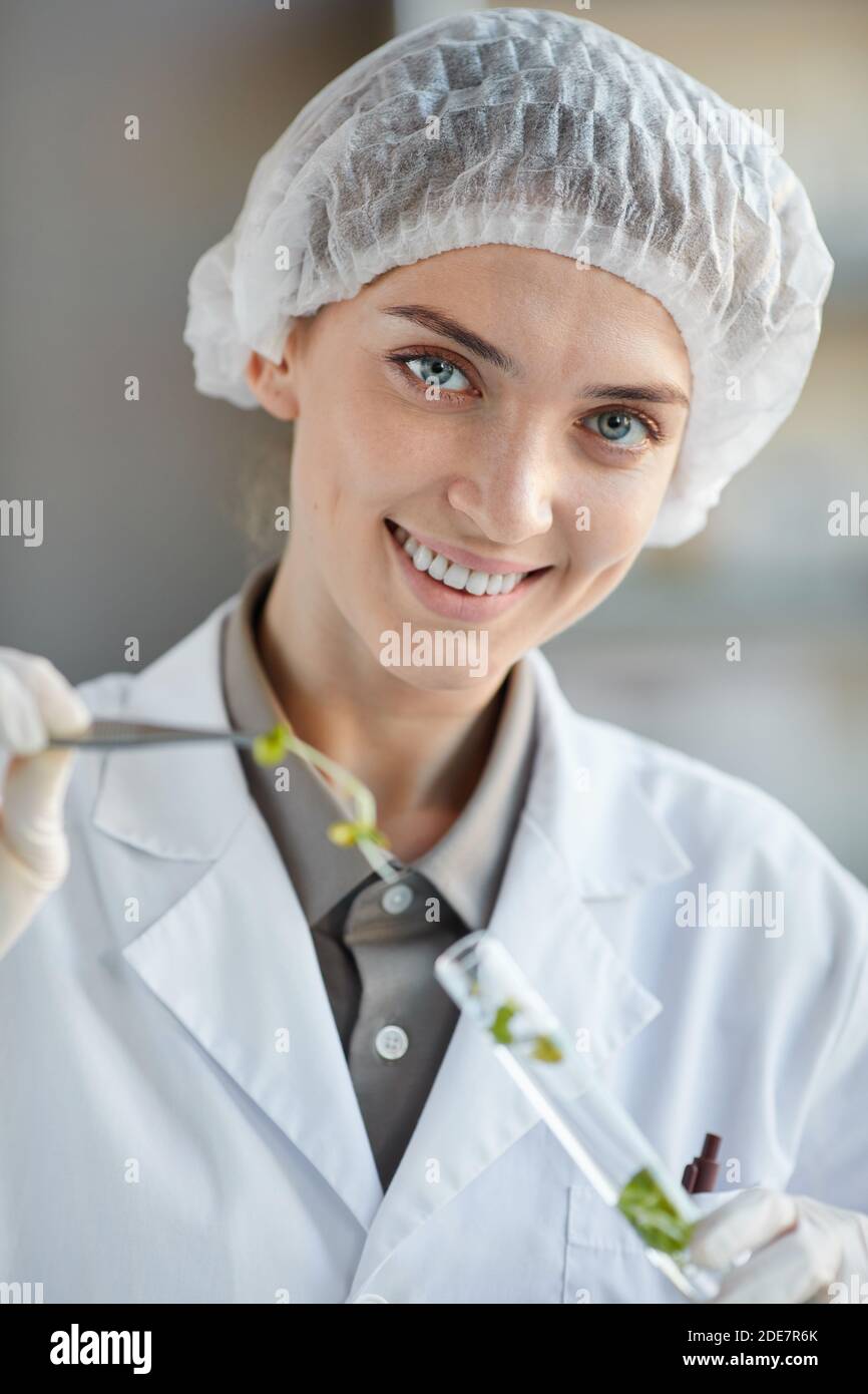 Vertical portrait of smiling female scientist holding test tube with plant samples while working on research in biotechnology lab Stock Photo
