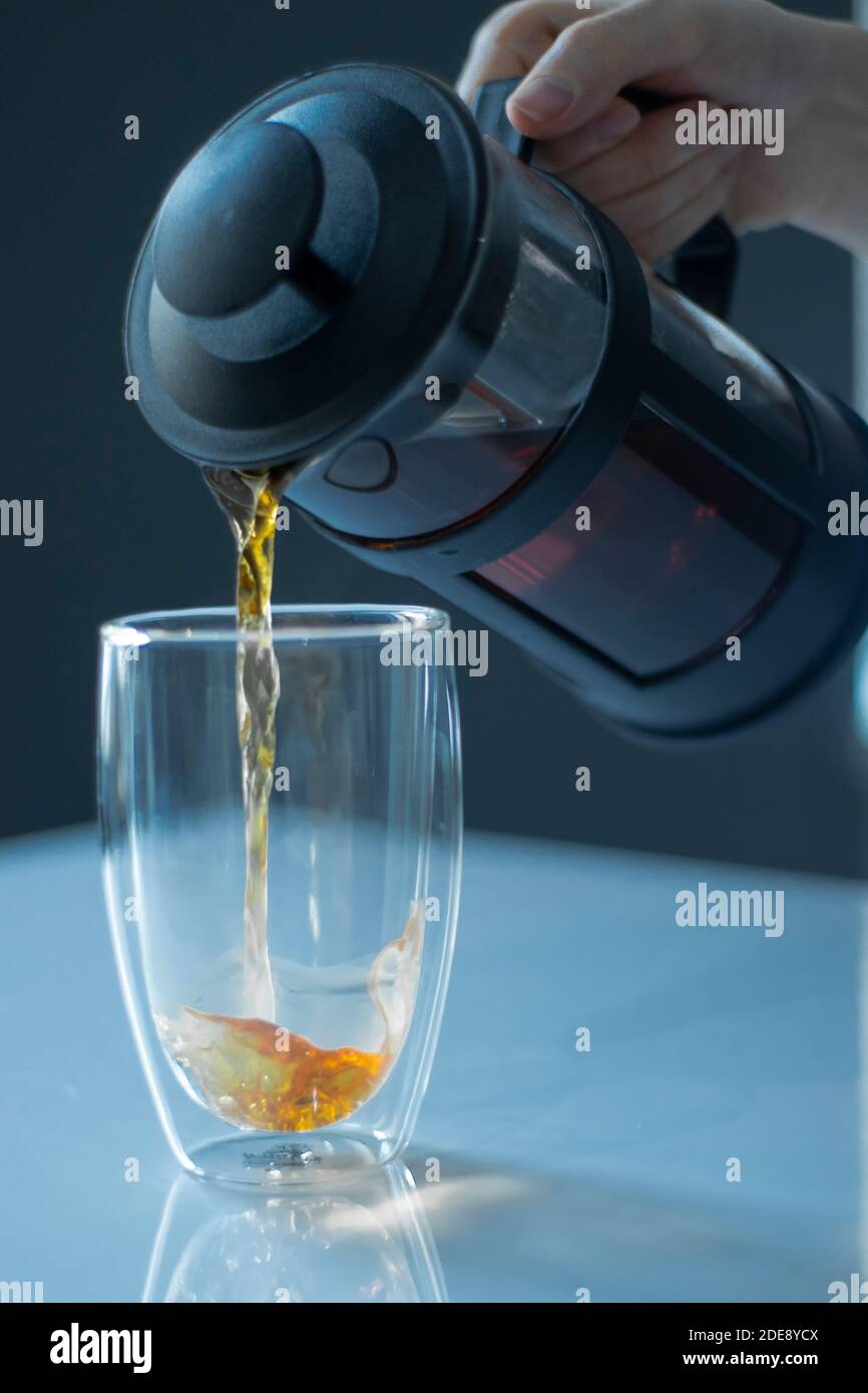 french press black tea pouring into a glass with a double bottom on a