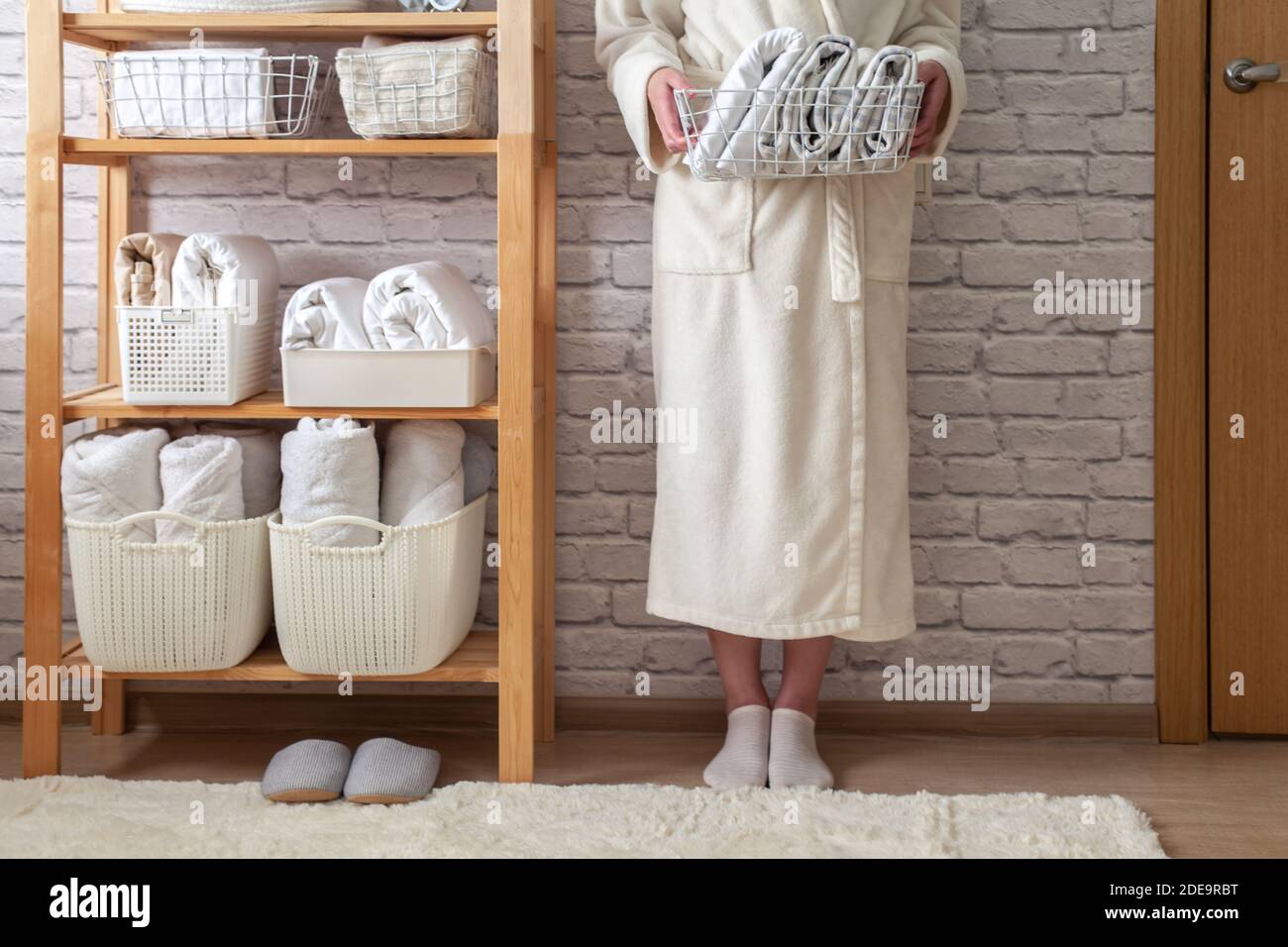 Woman in robe standing and holding white wire basket of folded bed