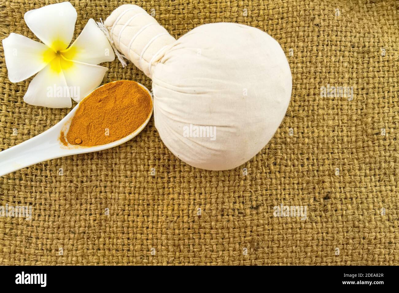 Spa herbal compressing ball , white frangipani flowers (Plumeria spp , Apocynaceae, Pagoda tree, Temple tree) and turmeric powder in wooden spoon on b Stock Photo