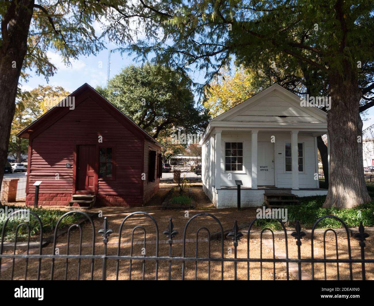 Old Wyatt Office, a Greek Revival building with columns, and the Calaboose, a former jail, in Waxahachie, Texas beneath deciduous trees. Stock Photo