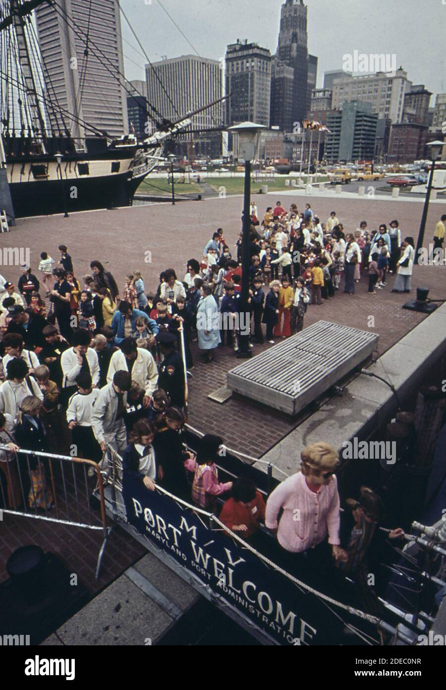 School children board the Port Welcome for a tour of Baltimore Harbor. U.S.S. Constitution and Baltimore skyscrapers in background ca. 1973 Stock Photo