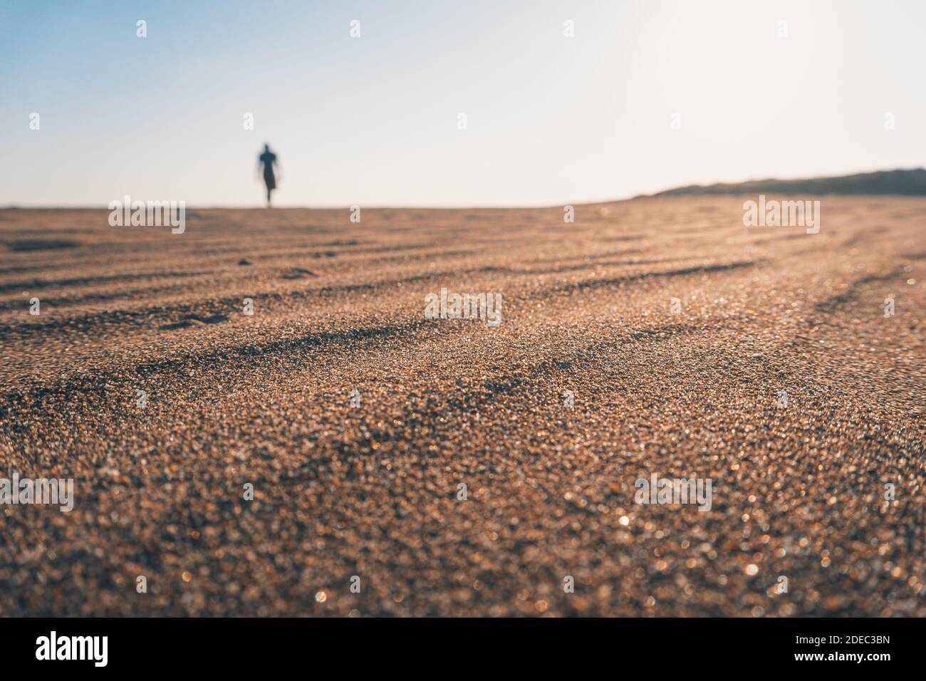Silhouette man walking on the beach at sunset. Close up wavy sand view. Summer and travel concept. Stock Photo