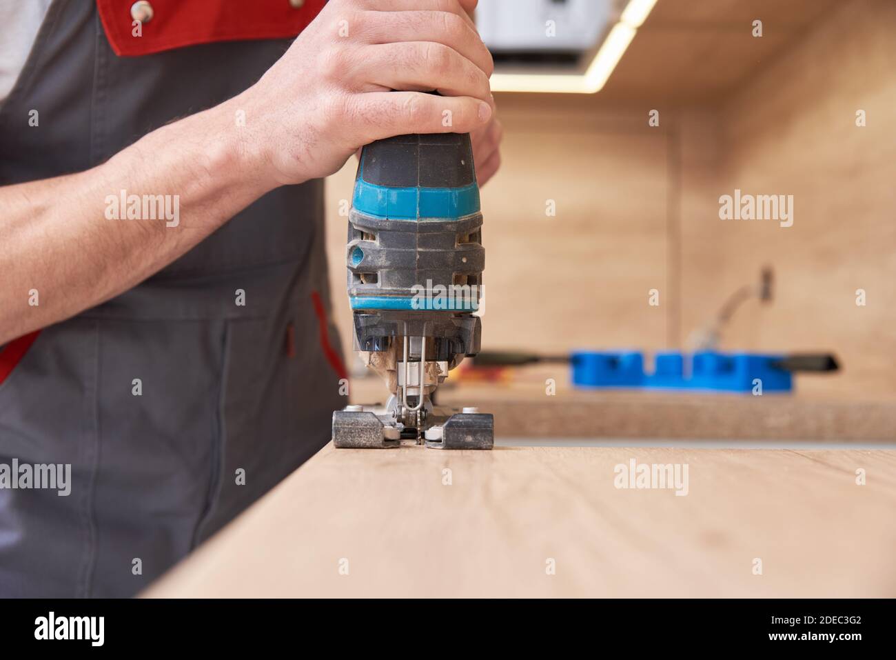 Repairman using electric jigsaw. Sawing place for installing gas hob in