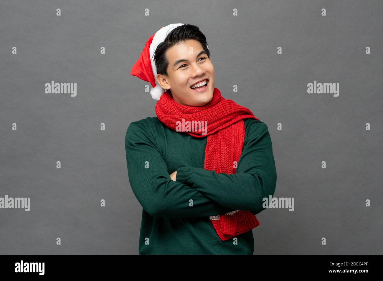 Smiling happy Asian man wearing colorful red and green Christmas theme clothes with arms crossed looking at copy space aside isolated on gray backgrou Stock Photo