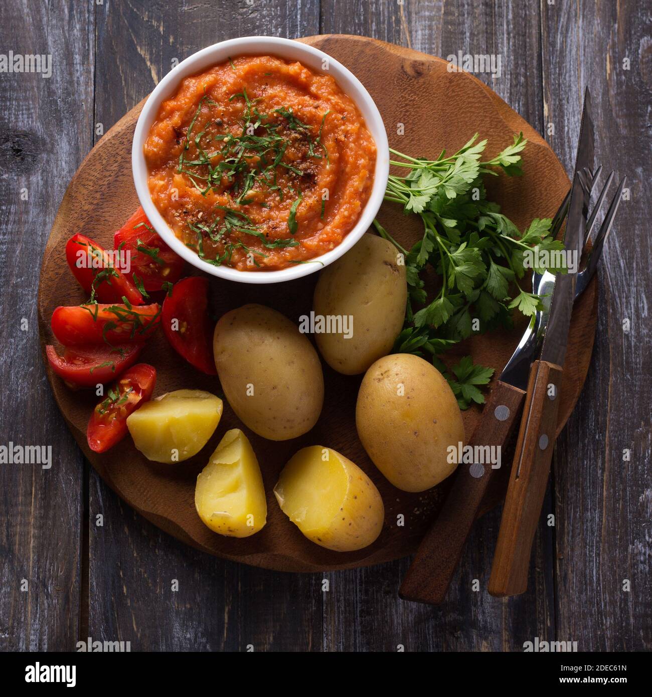 Young potatoes boiled in a peel with zucchini caviar or dip of vegetables, spices, fresh tomatoes and parsley on a wooden board. Simple healthy homema Stock Photo