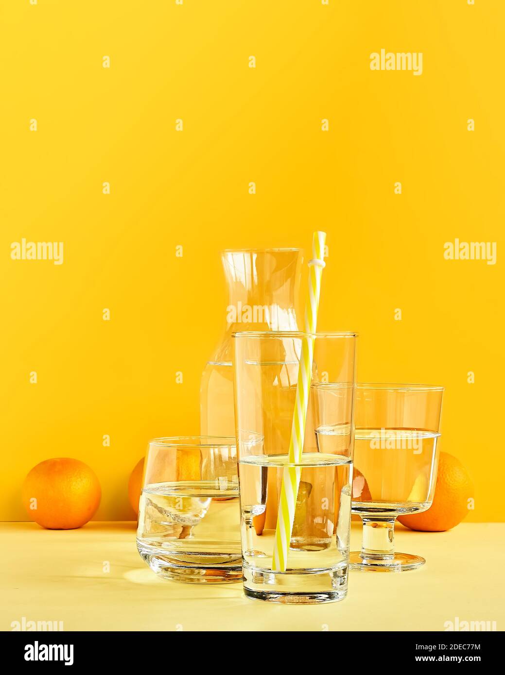 Citrus fruits distorted through water and glass on yellow background. Art trendy minimalist still life. Healthy lifestile. Vitamin C. Stock Photo