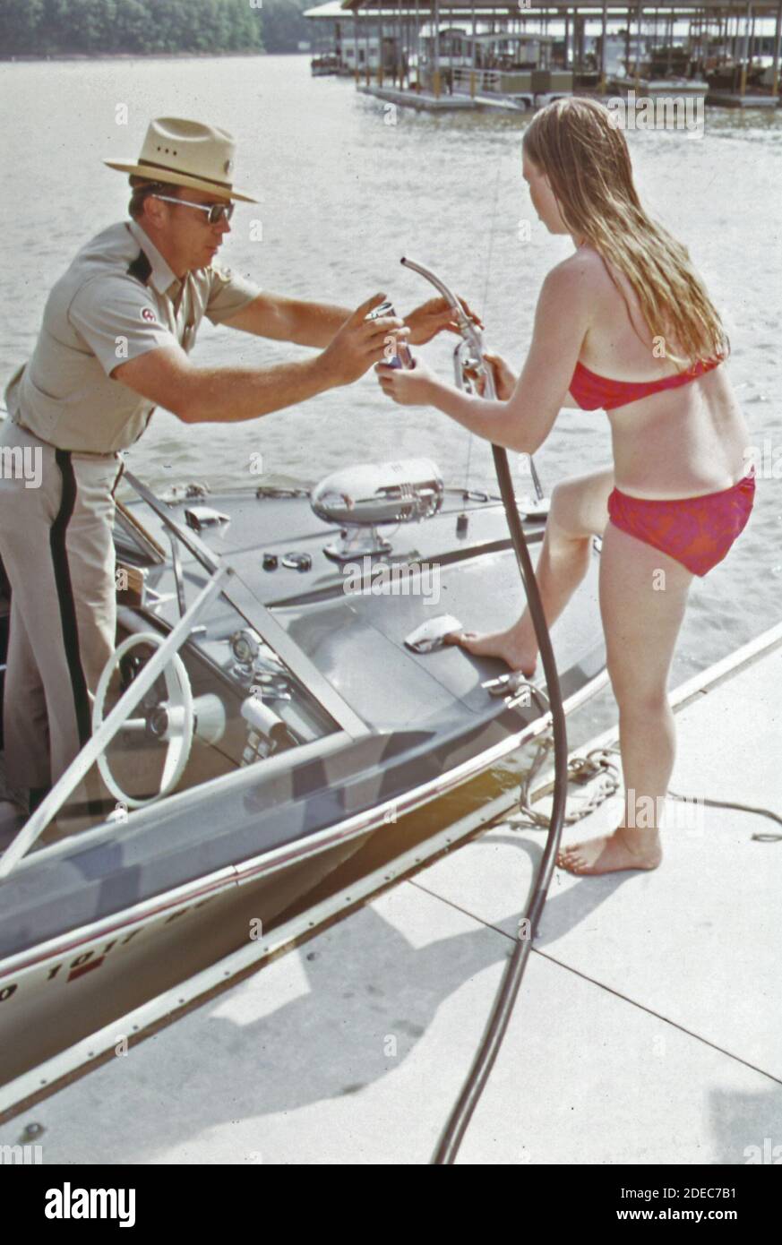1970s Photos (1973) -  Water patrol supervisor dan needham stops to refuel at Bikini Beach; a floating service station with a self-explanatory name. Attendant is jill phillips; a college student working summers  (Lake of the Ozarks Missouri area) Stock Photo