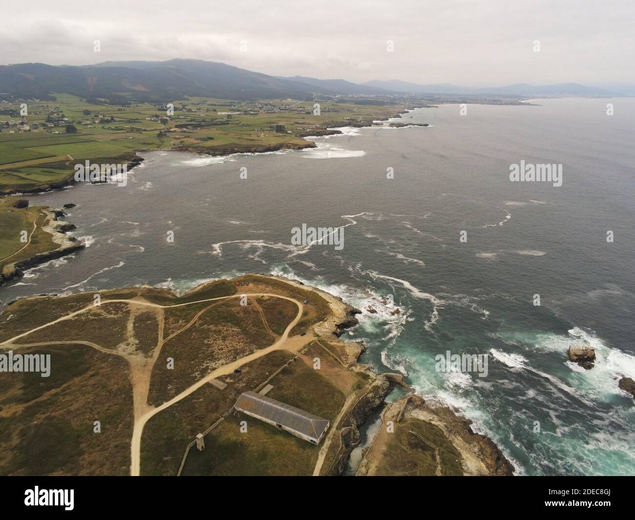 An aerial view of the wavy ocean hitting the rocky cliffs in Rinlo ...