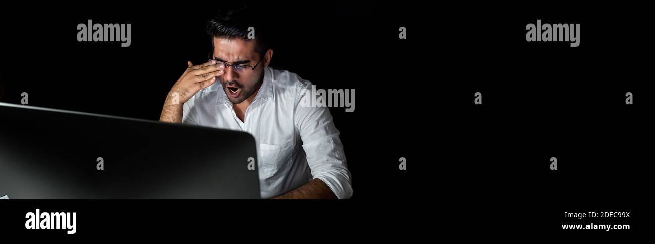 Tired fatigued Asian businessman feeling sleepy and yawning while working night shift in front of computer, panoramic banner with copy space Stock Photo