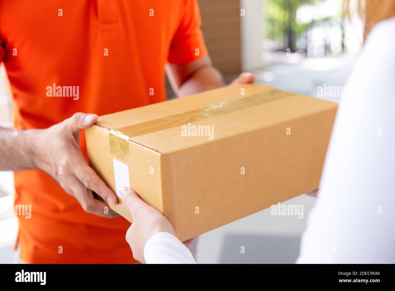 Courier service delivery man in orange uniform giving parcel box to customer at home Stock Photo