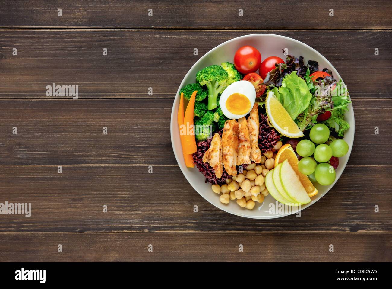 Clean healthy low fat ready to eat food with mixed vegetable and fruit salad in round shape dish on wood table background top view with copy space Stock Photo