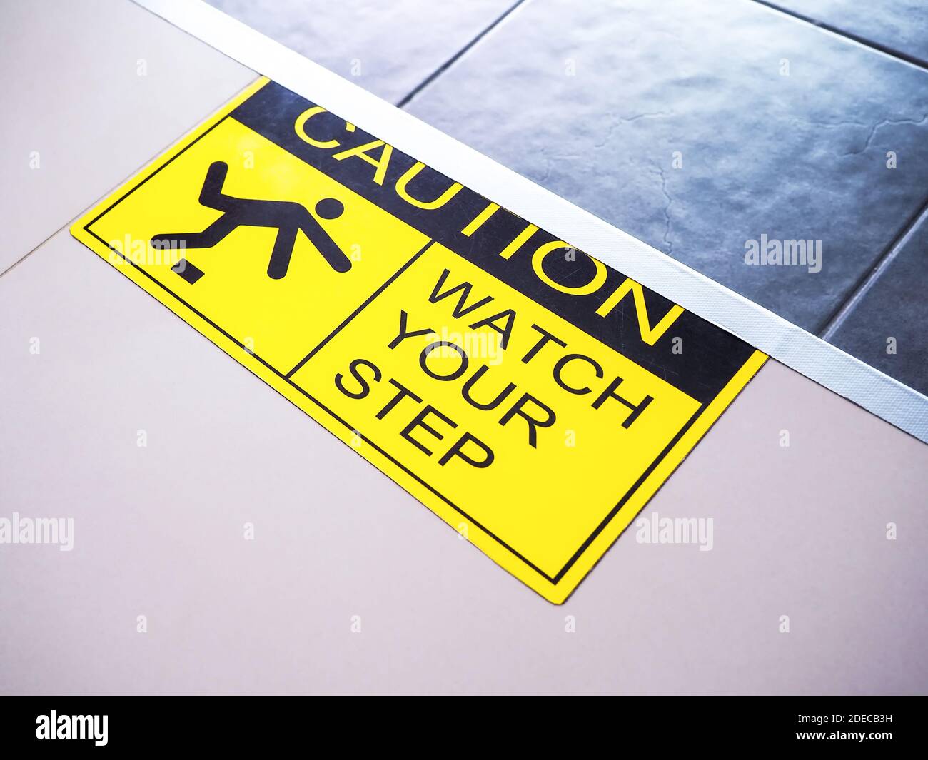 'Caution watch your step' on yellow and black warning sticker sign on the floor, warning and care when going up or down steps. Stock Photo