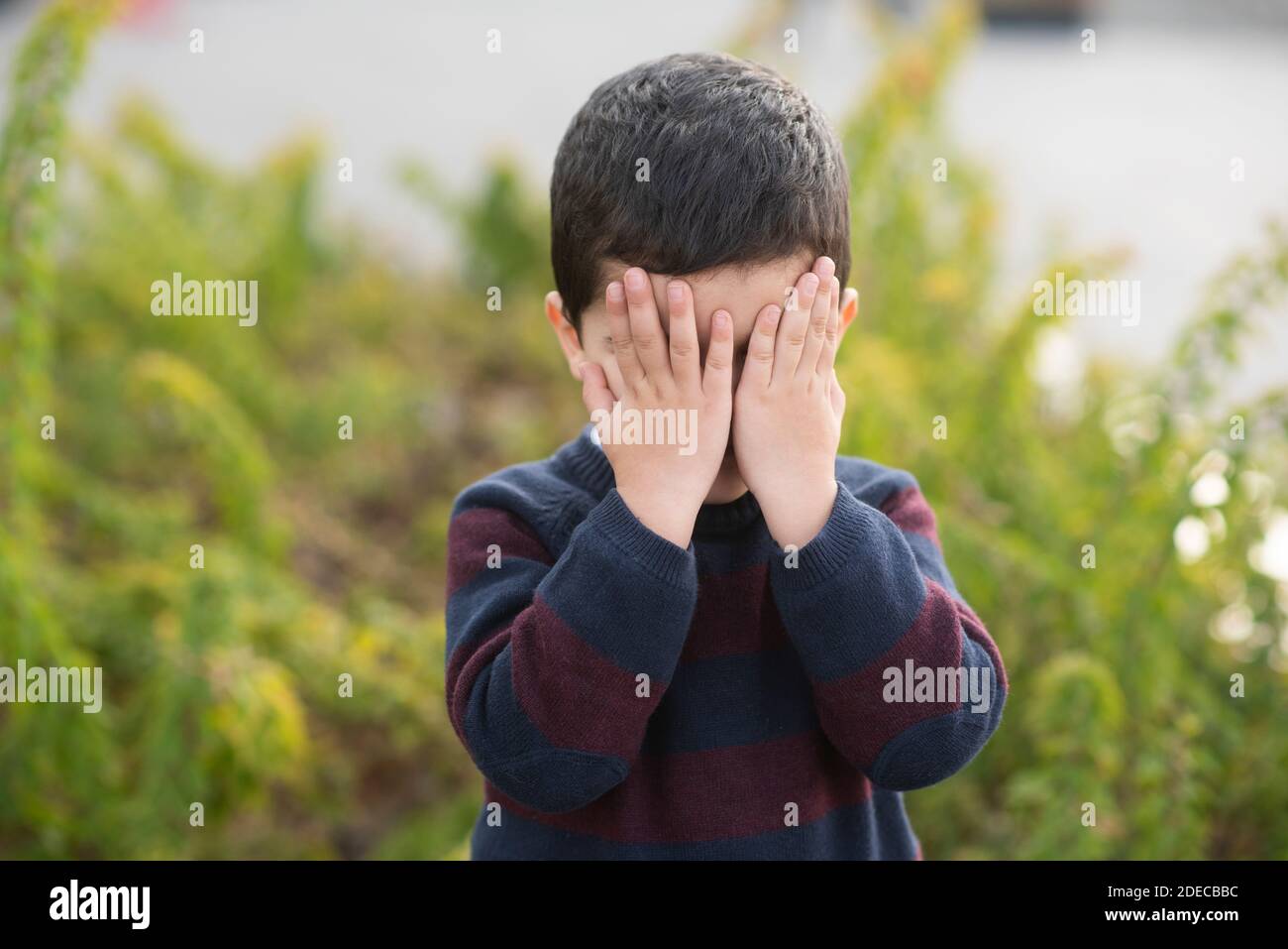 4 years old boy hiding face with hands outdoors Stock Photo