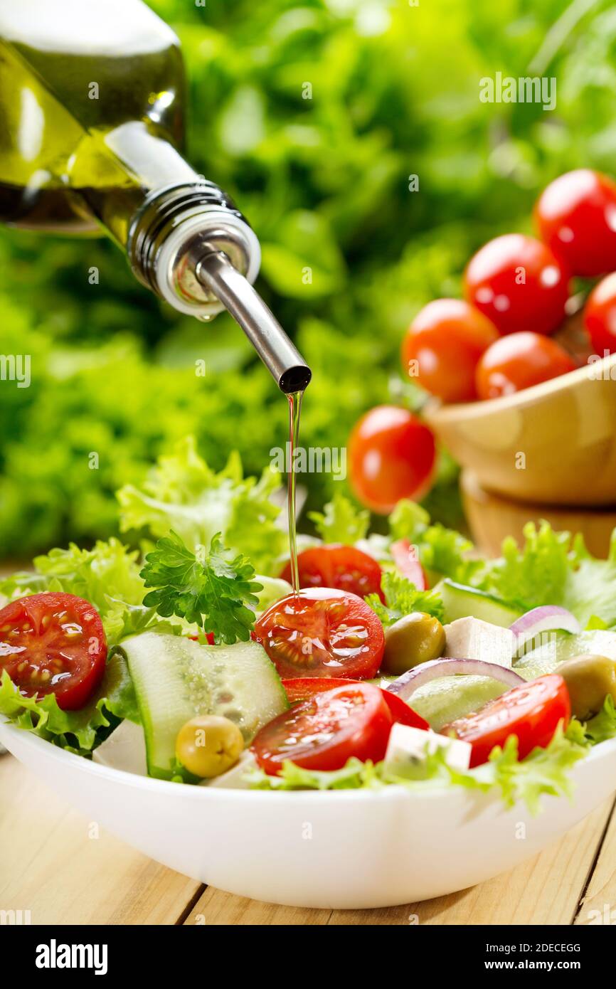 olive oil pouring into bowl of salad Stock Photo